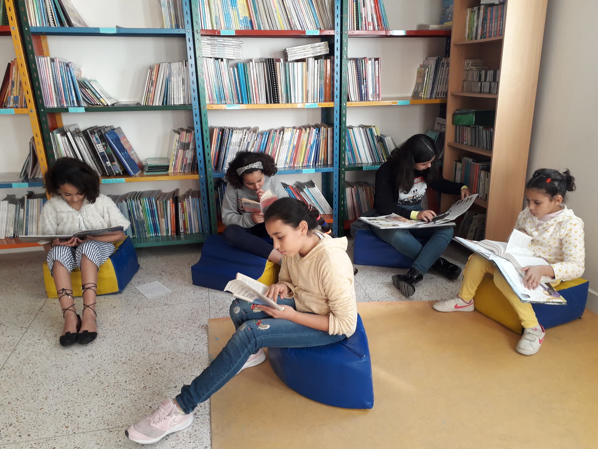 Élèves du primaire des Iris installés sur des poufs, en train de lire des livres et des revues à la bibliothèque de l’école